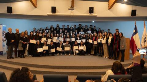 Un grupo de estudiantes y autoridades posan en un evento de entrega de certificados en un auditorio.