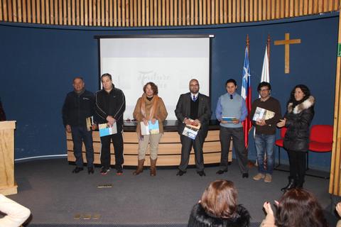 Un grupo de personas participa en un evento de premiación en un auditorio, con banderas y una cruz al fondo.