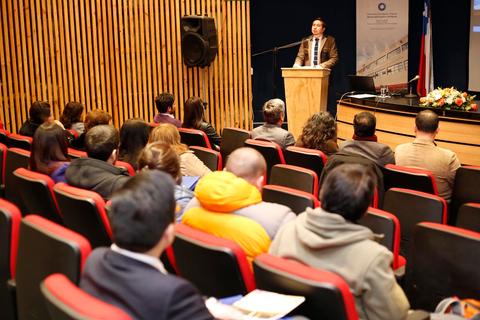 Un ponente da una charla en un auditorio con asistentes sentados.