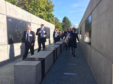 Un grupo de personas camina por un pasillo moderno con paredes de concreto y elementos decorativos.