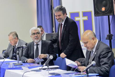 Cuatro hombres se sienten en una mesa durante una reunión, sonriendo y revisando documentos en un ambiente formal.
