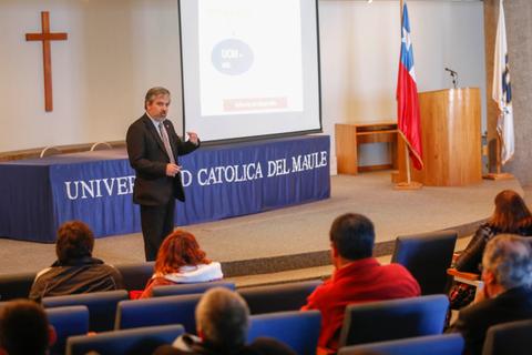 Un presentador habla frente a un grupo de personas en una sala de conferencias de la Universidad Católica del Maule.