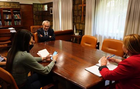 Una reunión en una sala con cuatro personas sentadas alrededor de una mesa grande, enfocándose en la conversación y tomando notas.