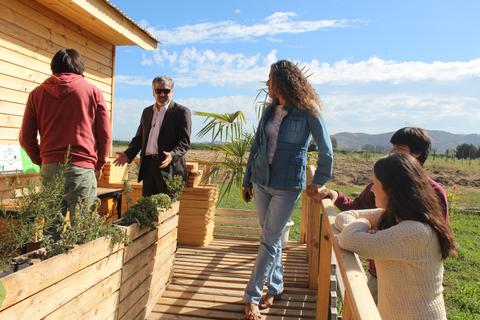 Un grupo de personas interactuando en una terraza de madera frente a una casa de campo.