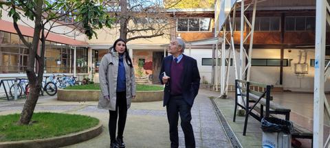 Dos personas conversan en un patio con árboles y bicicletas.
