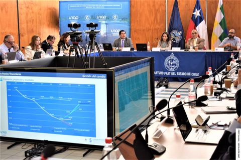 Reunión de un grupo de personas en una mesa de trabajo con gráficos y banderas de Chile.