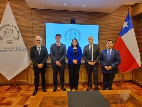 Un grupo de cinco personas posando en una sala de reuniones con banderas y un logotipo institucional de Chile en el fondo.