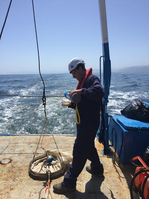 Un hombre trabaja en un barco en medio del mar, preparando un equipo de muestreo.