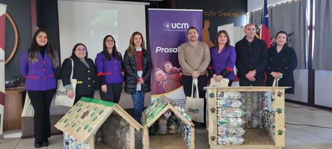 Un grupo de personas posando junto a casas hechas de botellas recicladas en un evento de concienciación ambiental.
