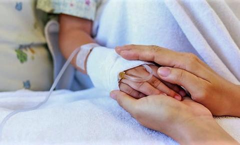 Un adulto sostiene la mano de un niño en un entorno hospitalario.