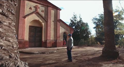 Un hombre observa una iglesia en un entorno natural con palmas alrededor.