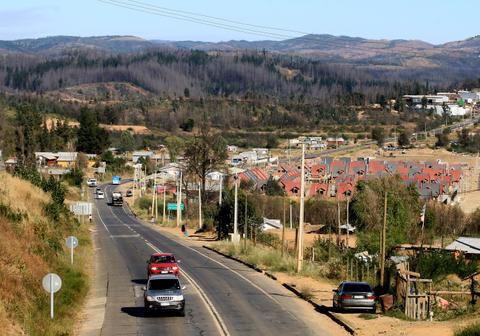 Una carretera que se extiende por un paisaje rural con casas y montañas al fondo.