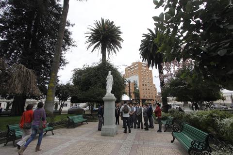 Una plaza con gente rodeada de árboles y una estatua en el centro.