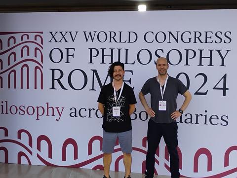 Dos personas posan frente a un cartel del XXV Congreso Mundial de Filosofía en Roma 2024.