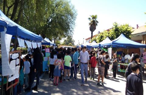 Una feria escolar con numerosos stands y un gran grupo de estudiantes reunidos.