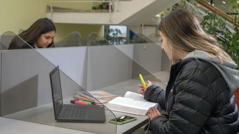 Dos estudiantes trabajando en un espacio de estudio con separadores de acrílico.