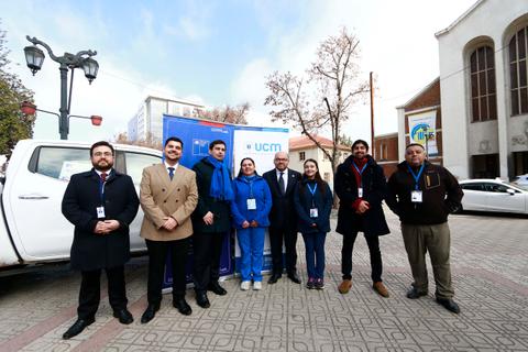 Un grupo de personas vestidas de manera formal y profesional, posando junto a un vehículo en un ambiente urbano.