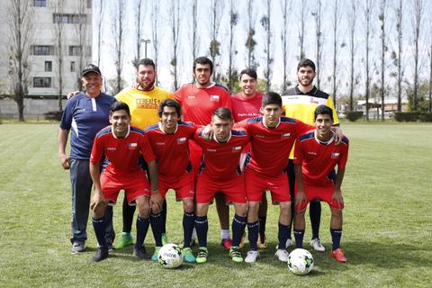 Un grupo de jugadores de fútbol posando en una cancha junto a un adulto mayor.