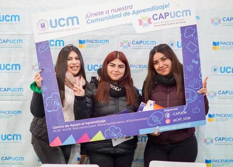 Tres jóvenes posan con un marco de fotografía en un evento de la Universidad Católica del Maule.