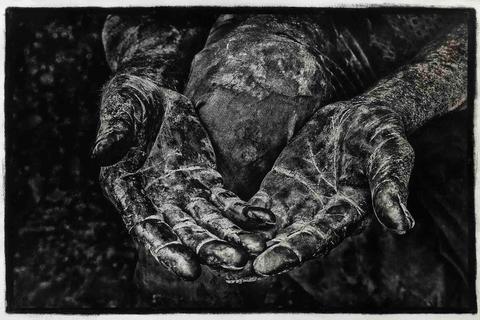 Las manos de una persona, cubiertas de una sustancia oscura y con una textura evidente, se presentan en un gesto de espera o entrega.