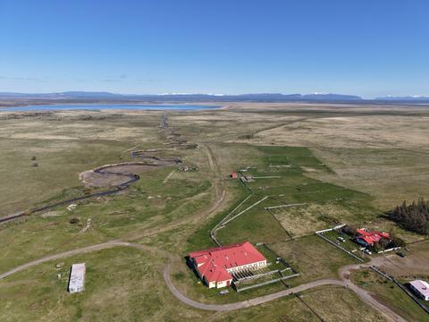 Una vista aérea de un paisaje natural con campos verdes y una construcción roja en el centro.