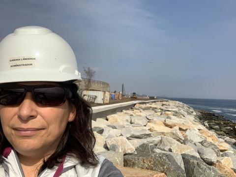 Mujer con casco y gafas de sol en un paseo marítimo junto al mar.