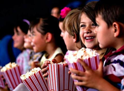 Un grupo de niños sonrientes disfruta de una película mientras sostienen cubos de palomitas.