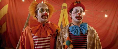 Dos payasos sonrientes posan en un ambiente circense colorido.