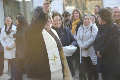 Un grupo de personas celebra un evento con un sacerdote que rocía agua bendita.