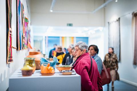 Un grupo de personas observa diversas piezas de cerámica y arte en una galería.