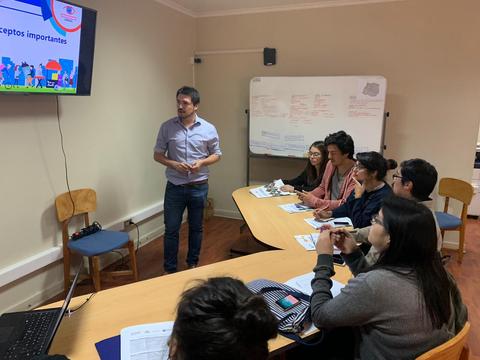 Un grupo de personas está en una sala de clases escuchando a un instructor que presenta información en una pantalla.