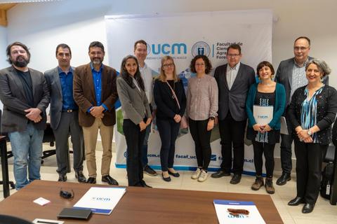 Un grupo de personas posando frente a un banner de la universidad en una sala de reuniones.