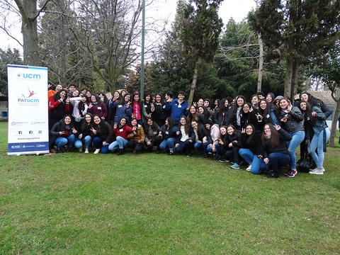 Un grupo grande de personas posando juntas en un parque con un cartel de fondo.