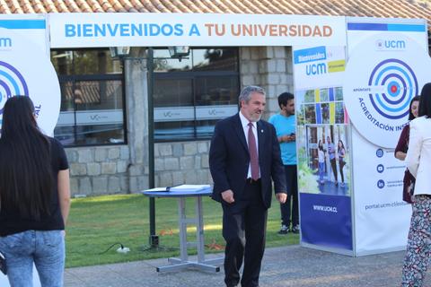 Un evento de bienvenida a la universidad con un hombre de traje y diversas personas en el fondo.