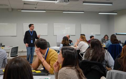 Un grupo de personas escucha a un hombre que está dando una presentación en un aula moderna.