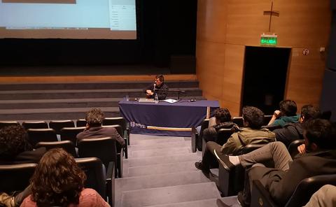 Una charla en un auditorio con un ponente frente a una audiencia sentada.