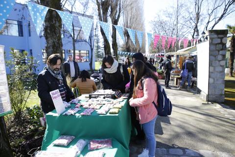Una feria al aire libre con personas comprando en un puesto lleno de productos variados.