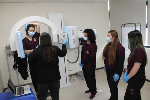 Un grupo de estudiantes de salud observa la realización de un examen de mamografía en una sala de diagnóstico.