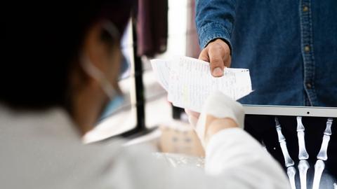 Una persona entrega documentos a un profesional de la salud mientras se observa una radiografía.