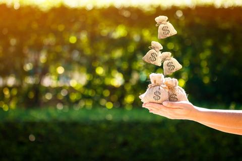 Una mano sostiene varios sacos de dinero que parecen flotar en el aire.