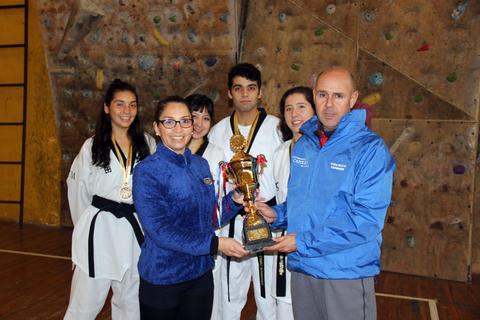 Un grupo de artistas marciales posando con un trofeo en un gimnasio.