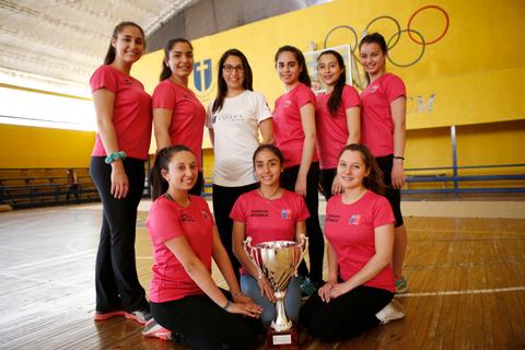 Un grupo de jóvenes atletas sonríen junto a un trofeo en un gimnasio.
