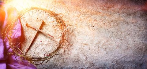 La imagen muestra una corona de espinas y una cruz sobre una superficie rugosa iluminada por la luz del sol.