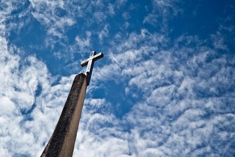 Una cruz se alza sobre un hermoso cielo azul con nubes blancas.