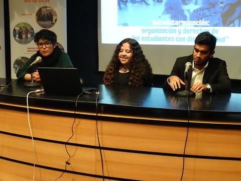 Tres personas sentadas en una mesa durante un evento, discutiendo sobre los derechos de los estudiantes con discapacidad.