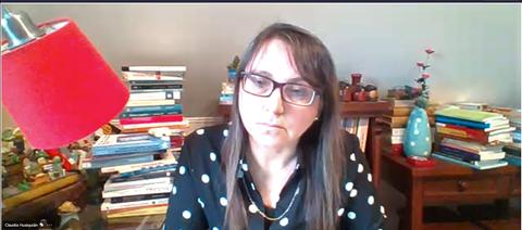 Una mujer con gafas y una blusa de círculos negros está sentada frente a una mesa llena de libros y decoraciones.