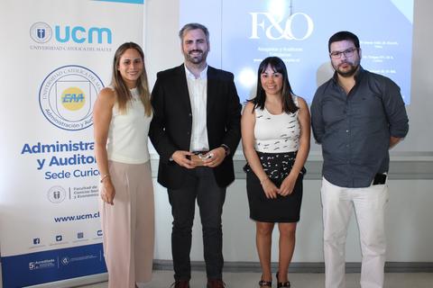 Cuatro personas posan frente a un cartel de la Universidad Católica del Maule.