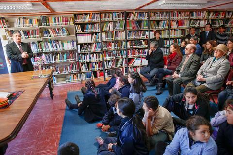 Un orador se dirige a un grupo de personas reunidas en una biblioteca.