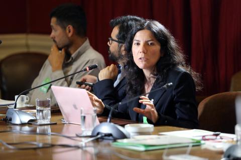 Una mujer habla en una mesa de discusión mientras otros dos hombres la escuchan atentamente.