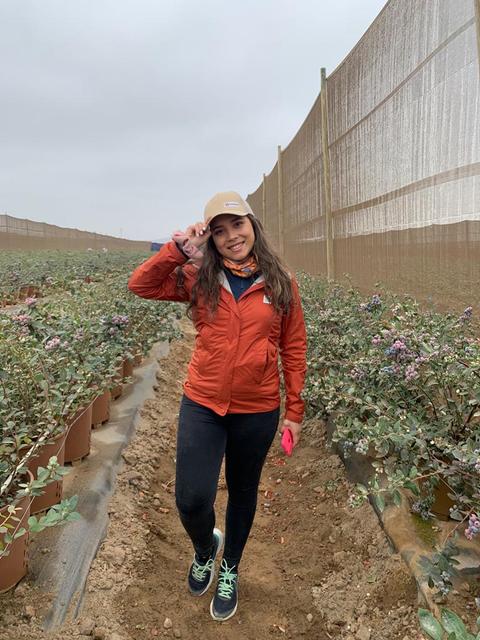 Una mujer sonriente en un campo rodeado de plantas en macetas.